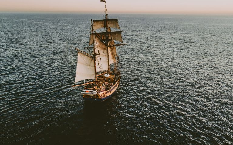 An old ship sails across an open ocean. 