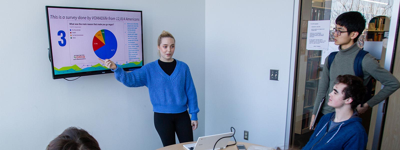 Student giving a presentation on a television monitor in a library study room.