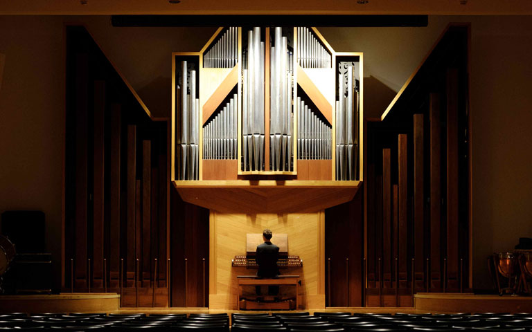 A person is seated facing an organ, ready to play the large instrument.