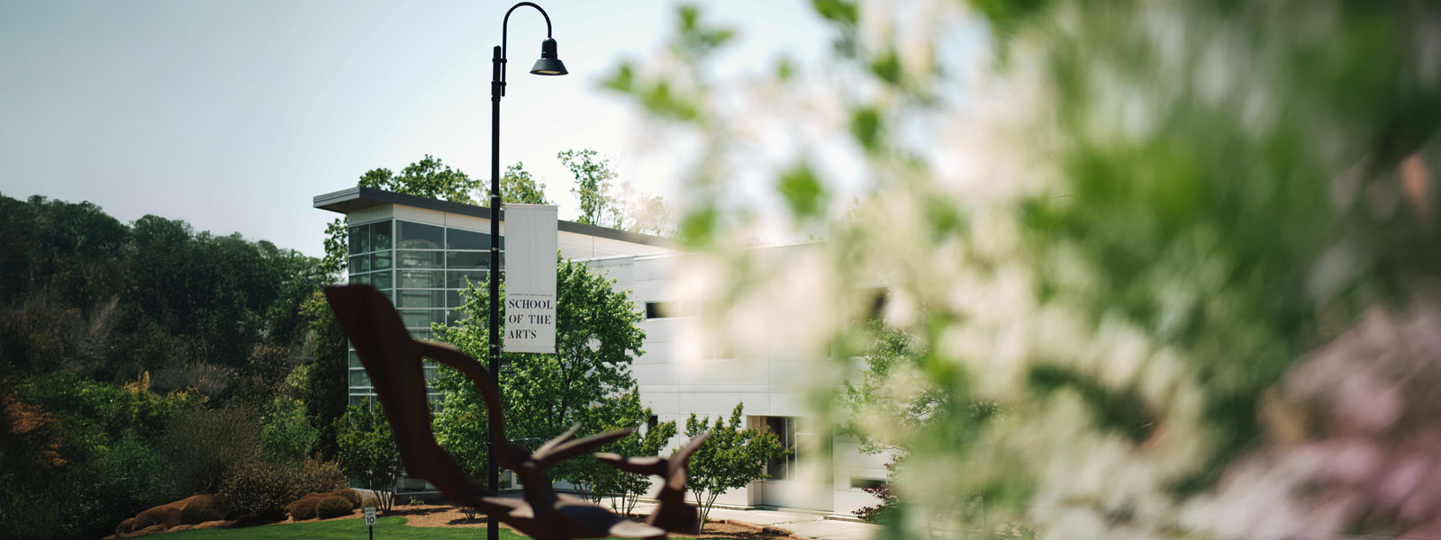 A sculpture is positioned on a bench, with a building in the background, blending art and architecture.