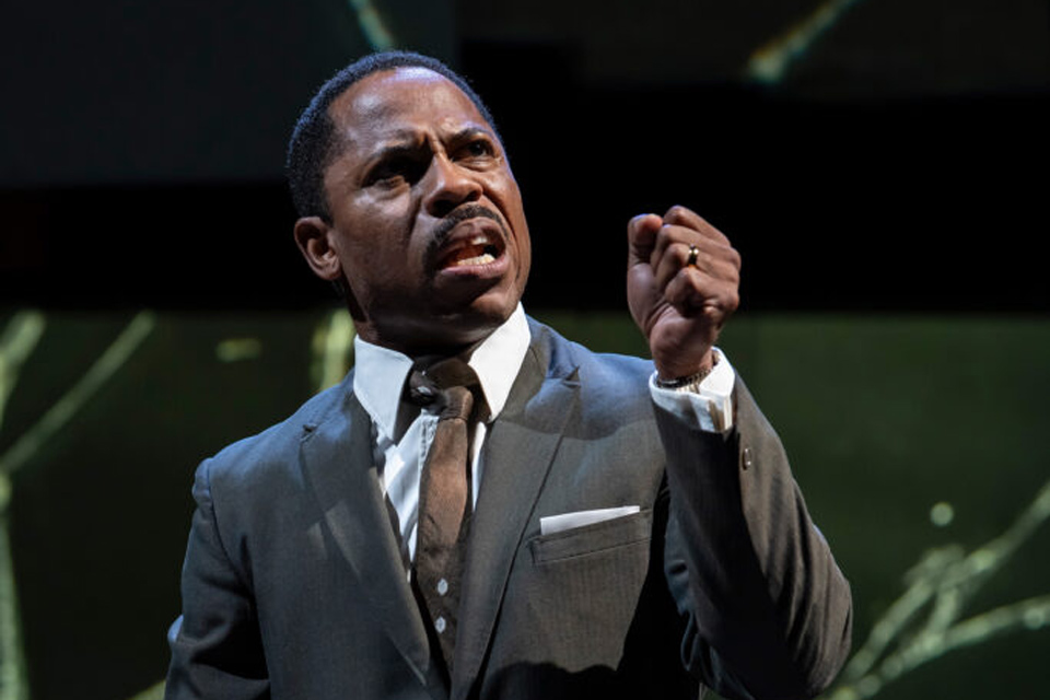  A man in a suit and tie is delivering a speech at a podium, engaging with the audience.