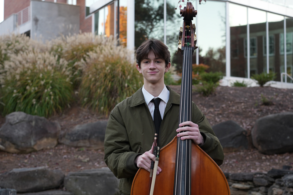 A young boy stands smiling with a double bass.